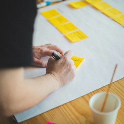 Person writing ideas on a large sheet covered with sticky notes during a workshop.